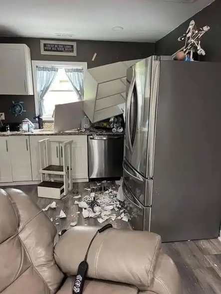 A homeowner holding a heavy kitchen cabinet against a wall, demonstrating the need for secure mounting.